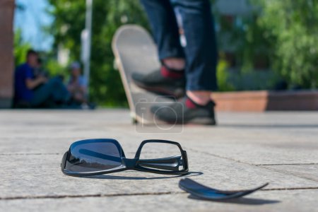 Téléchargez les photos : Lunettes de soleil cassées skateboarder, couché sur l'asphalte - en image libre de droit