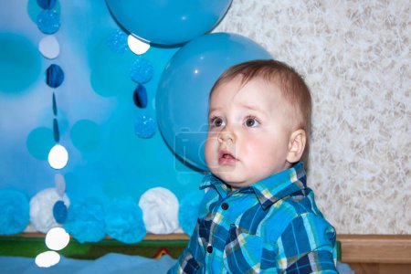 Téléchargez les photos : Un beau bébé fête son premier anniversaire. Portrait du bébé. Un garçon en chemise bleue parmi les ballons et les cadeaux. - en image libre de droit