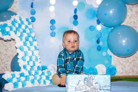 Foto de Un hermoso bebé está celebrando su primer cumpleaños. Retrato del bebé. Un niño con una camisa azul entre globos y regalos. - Imagen libre de derechos
