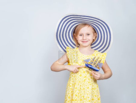 Foto de "Una chica con un sombrero de ala ancha sostiene un bote de juguete en sus manos." - Imagen libre de derechos