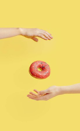 Photo for "Donut falls between hands on yellow background" - Royalty Free Image