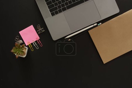 Foto de Escritorio de negocios con computadora portátil y papel memo colocado sobre un fondo negro, incluyendo un área de copia para agregar texto o gráficos - Imagen libre de derechos