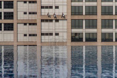 Photo for Group of workers cleaning windows service on high rise office building with reflection fiom swimming pool. - Royalty Free Image