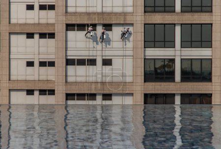 Foto de Group of workers cleaning windows service on high rise office building with reflection fiom swimming pool. - Imagen libre de derechos