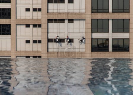 Foto de Grupo de trabajadores servicio de limpieza de ventanas en edificio de oficinas de gran altura con piscina fiom reflexión. - Imagen libre de derechos
