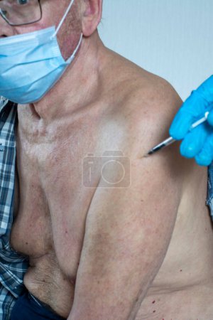 Photo for "A syringe in his hand with a vaccine and a patient is an old man. Indoors in daylight. Front view." - Royalty Free Image
