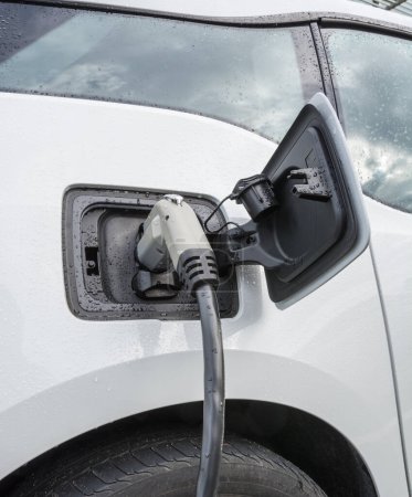 Photo for "Electric vehicle with the power plug connected to the car" - Royalty Free Image
