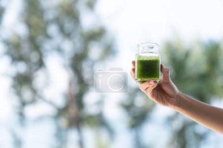Téléchargez les photos : "Woman hand holding a green smoothies on garden background. Healthy smoothies." - en image libre de droit