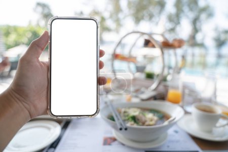 Téléchargez les photos : Woman hands holding blank screen mockup phone, order food online concept, breakfast background. - en image libre de droit