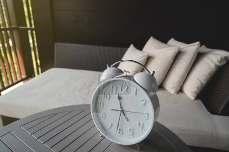 Photo for White alarm clock stands on a table next to the bed. - Royalty Free Image