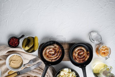 Foto de "Wurst or Bratwurst with Fermented Cabbage, Pickled Cucumbers, and Spices in cast iron frying pan, on white background, top view flat lay , with space for text copyspace" - Imagen libre de derechos