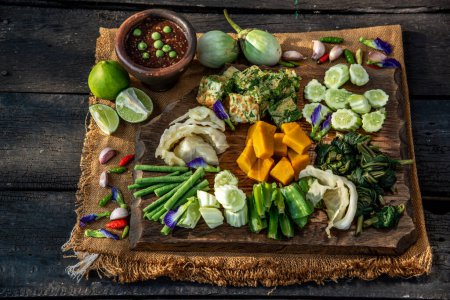 Téléchargez les photos : Alimentation traditionnelle thaïlandaise : Trempette de pâte de crevettes épicée ou sauce de pâte de crevettes frites (Nam Prik Kapi) avec légumes blanchis et omelettes cha-om sur fond en bois - en image libre de droit