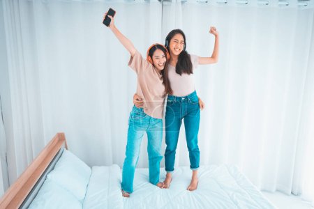 Foto de Felices mujeres amigables divirtiéndose en casa, saltando en la cama - Imagen libre de derechos