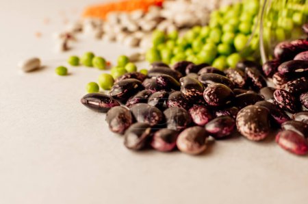 Foto de "A set of different dried legumes is in glass cups and is a little scattered: red lentils, green peas, red beans, white beans. Selective Focus on Red Beans" - Imagen libre de derechos