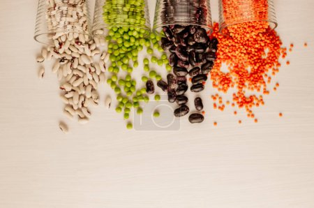Téléchargez les photos : "A set of different dried legumes is in glass cups and is a little scattered: red lentils, green peas, red beans, white beans. Legumes at the top of the frame and copy space." - en image libre de droit