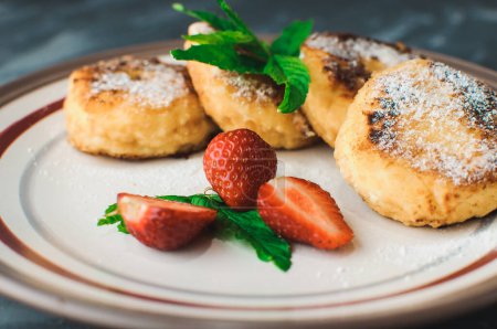 Photo for "Gourmet breakfast - curd pancakes, cheesecakes, curd pancakes with strawberries, mint and icing sugar in a white plate. Selective focus." - Royalty Free Image