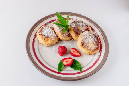 Photo for "Gourmet breakfast - cottage cheese pancakes, cheesecakes, cottage cheese pancakes with strawberries, mint and powdered sugar in a white plate. Useful dessert on white background isolate" - Royalty Free Image