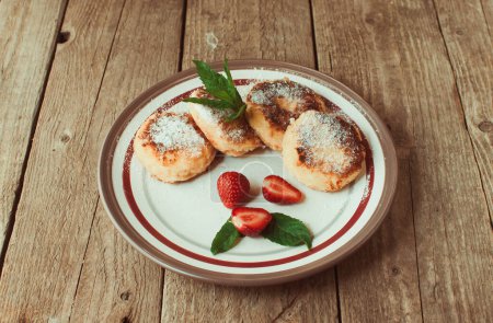 Foto de "Gourmet breakfast - cottage cheese pancakes, cheesecakes, cottage cheese pancakes with strawberries, mint and powdered sugar in a white plate. Selective focus." - Imagen libre de derechos