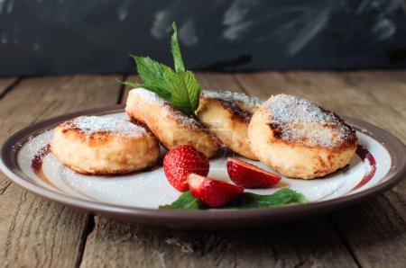 Photo for "Gourmet breakfast - cottage cheese pancakes, cheesecakes, cottage cheese pancakes with strawberries, mint and powdered sugar in a white plate. Selective focus." - Royalty Free Image