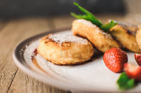Photo for "Gourmet breakfast - cottage cheese pancakes, cheesecakes, cottage cheese pancakes with strawberries, mint and powdered sugar in a white plate. Selective focus." - Royalty Free Image