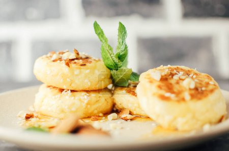 Foto de "Tartas de queso, tortitas de requesón con almendras, menta fresca y jarabe de arce sobre un fondo gris de una mesa de hormigón. Tartas de queso, caseras tradicionales ucranianas y rusas tartas de queso" - Imagen libre de derechos