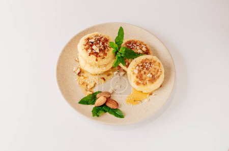 Foto de "Delicious breakfast - cottage cheese pancakes, cheesecakes, cottage cheese pancakes with almonds, mint and maple syrup in a beige plate. Useful dessert on white background isolate" - Imagen libre de derechos