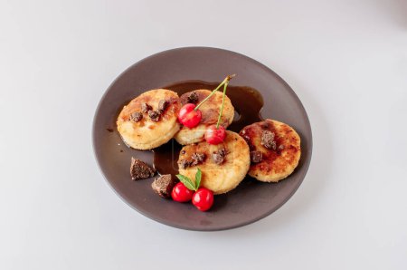 Foto de "Gourmet breakfast - curd pancakes, cheesecakes, curd pancakes with cherries and chocolate in a brown plate. Healthy dessert on a white background isolate" - Imagen libre de derechos