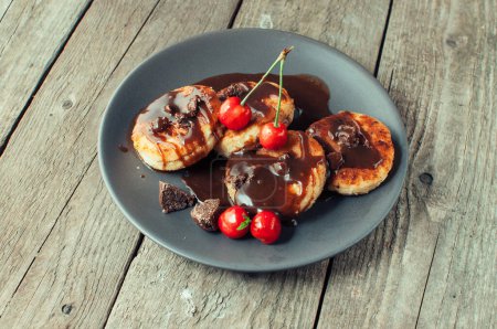 Foto de "Gourmet breakfast - curd pancakes, cheesecakes, curd pancakes with cherries and chocolate in a brown plate. Wholesome dessert on a wooden table in a rustic style. Selective focus" - Imagen libre de derechos