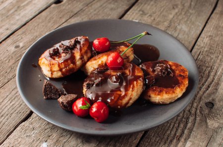 Photo for "Gourmet breakfast - curd pancakes, cheesecakes, curd pancakes with cherries and chocolate in a brown plate. Wholesome dessert on a wooden table in a rustic style. Selective focus" - Royalty Free Image