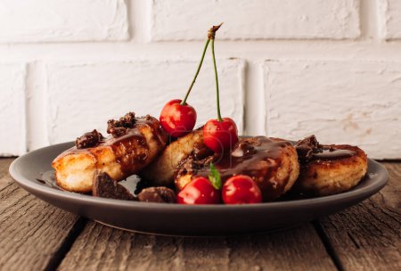 Téléchargez les photos : "Breakfast Food Tasty Concept. Cheesecakes, cheesecakes, curd pancakes with cherries and chocolate on a black background from a concrete table and a white brick wall. Close-up.Healthy Food" - en image libre de droit