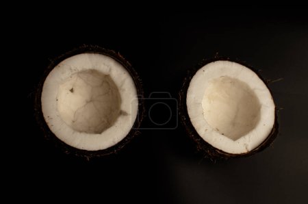 Téléchargez les photos : "laid noix de coco biologique sur fond noir, isoler. une noix cassée dans une coquille l'intérieur blanc d'une noix de coco, qui a commencé à se décomposer et recouvert de champignons et de moisissures. Produits gâtés
." - en image libre de droit