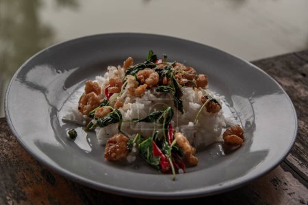 Photo for "Rice topped with Stir fried thai basil with dwarf prawn served in white dish on wooden table, Thai Style food." - Royalty Free Image