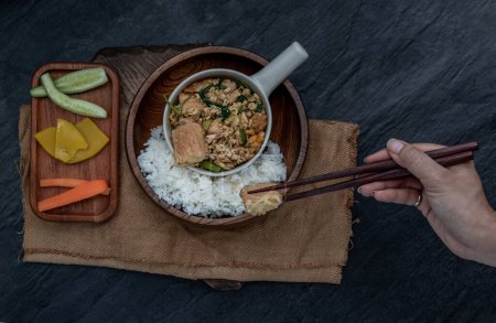 Foto de "La mano está usando palillos para recoger el tofu de huevo frito con cebolla de primavera con hierbas vegetales servidas con arroz al vapor en un tazón de madera." - Imagen libre de derechos