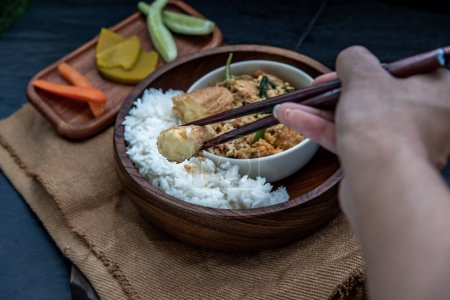 Foto de "The hand is using chopsticks to pick up  Stir fried egg tofu with spring onion with Herbs vegetables served with steamed rice in wooden bowl." - Imagen libre de derechos