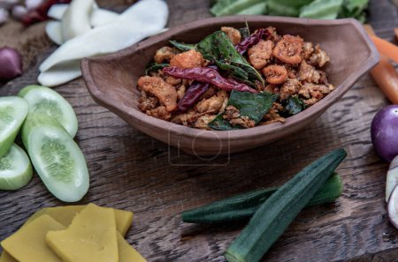 Photo for "Pork Crackling Chili Paste with fried kaffir lime leaves with the ingredient and fresh vegetables on wood background." - Royalty Free Image