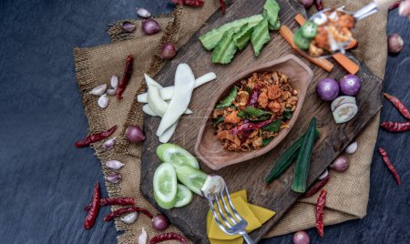 Photo for "Pork Crackling Chili Paste with fried kaffir lime leaves with the ingredient and fresh vegetables on wood background." - Royalty Free Image