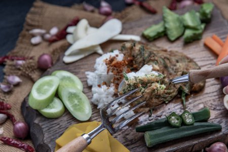 Téléchargez les photos : "Un style alimentaire thaïlandais local, La main utilise une cuillère pour ramasser l'omelette de pennata d'acacia frite ou les œufs cha-om sur du riz jasmin avec l'ingrédient et des légumes frais sur un fond en bois, " - en image libre de droit