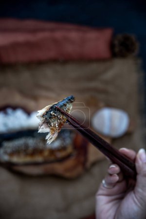 Photo for The hand is using chopsticks to pick up saba fish grilled on rice with teriyaki sauce on a sackcloth background. - Royalty Free Image