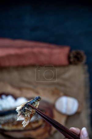 Foto de The hand is using chopsticks to pick up saba fish grilled on rice with teriyaki sauce on a sackcloth background. - Imagen libre de derechos