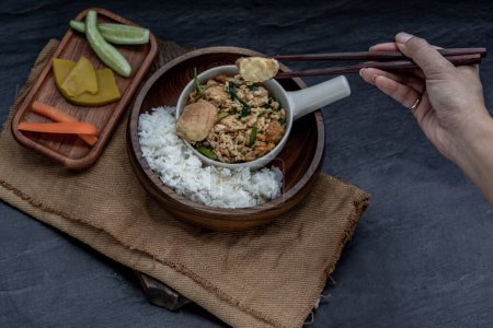Téléchargez les photos : "The hand is using chopsticks to pick up  Stir fried egg tofu with spring onion with Herbs vegetables served with steamed rice in wooden bowl." - en image libre de droit