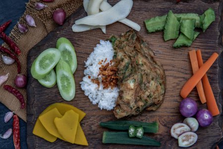 Foto de "A local Thai food style, Fried acacia pennata omelet or cha-om eggs on jasmine rice with the ingredient and fresh vegetables on a wooden background, Thai Cuisine." - Imagen libre de derechos