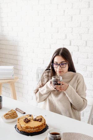 Foto de "Mujer joven bebiendo café negro caliente sentado en la mesa blanca" - Imagen libre de derechos