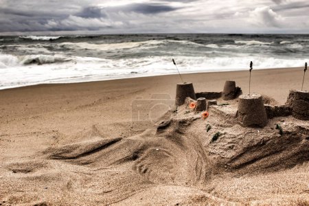 Téléchargez les photos : "Château de sable, Brave océan, formations rocheuses et ciel nuageux sur la plage" - en image libre de droit