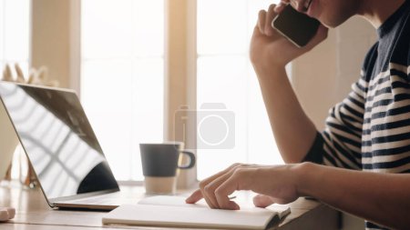 Photo for "man sitting at table looking pointing at computer screen discuss application talking on mobile phone working at home solve business issues distantly, self-employed male speak with client" - Royalty Free Image