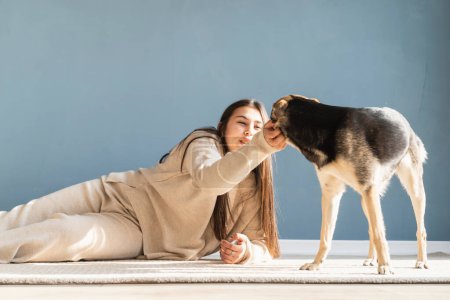 Photo for "Beautiful woman with playful dog embracing at home" - Royalty Free Image
