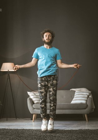 Photo for "A young man jumps on a rope at home. The quarantine pandemic sports concept. High quality photo" - Royalty Free Image
