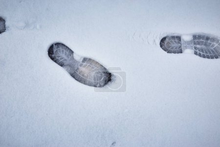 Téléchargez les photos : Marques de chaussures dans la neige fondante sur le fond de la chaussée asphaltée - en image libre de droit
