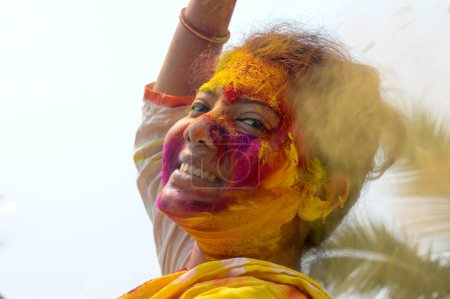 Foto de Retrato de una mujer joven india feliz con pintura en polvo de color rosa, amarillo y rojo Holi en la cara durante el festival Holi Color. Vista frontal. Mirando la cámara. - Imagen libre de derechos
