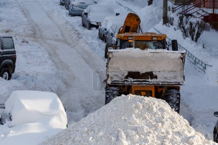 Foto de Tractor quitando nieve del estacionamiento cerca del edificio residencial en el día de invierno - Imagen libre de derechos