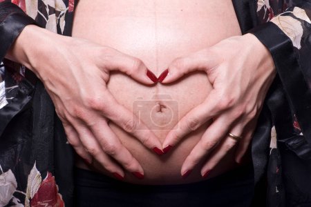 Foto de Manos formando el corazón en el vientre de la mujer embarazada estudio de rodaje - Imagen libre de derechos